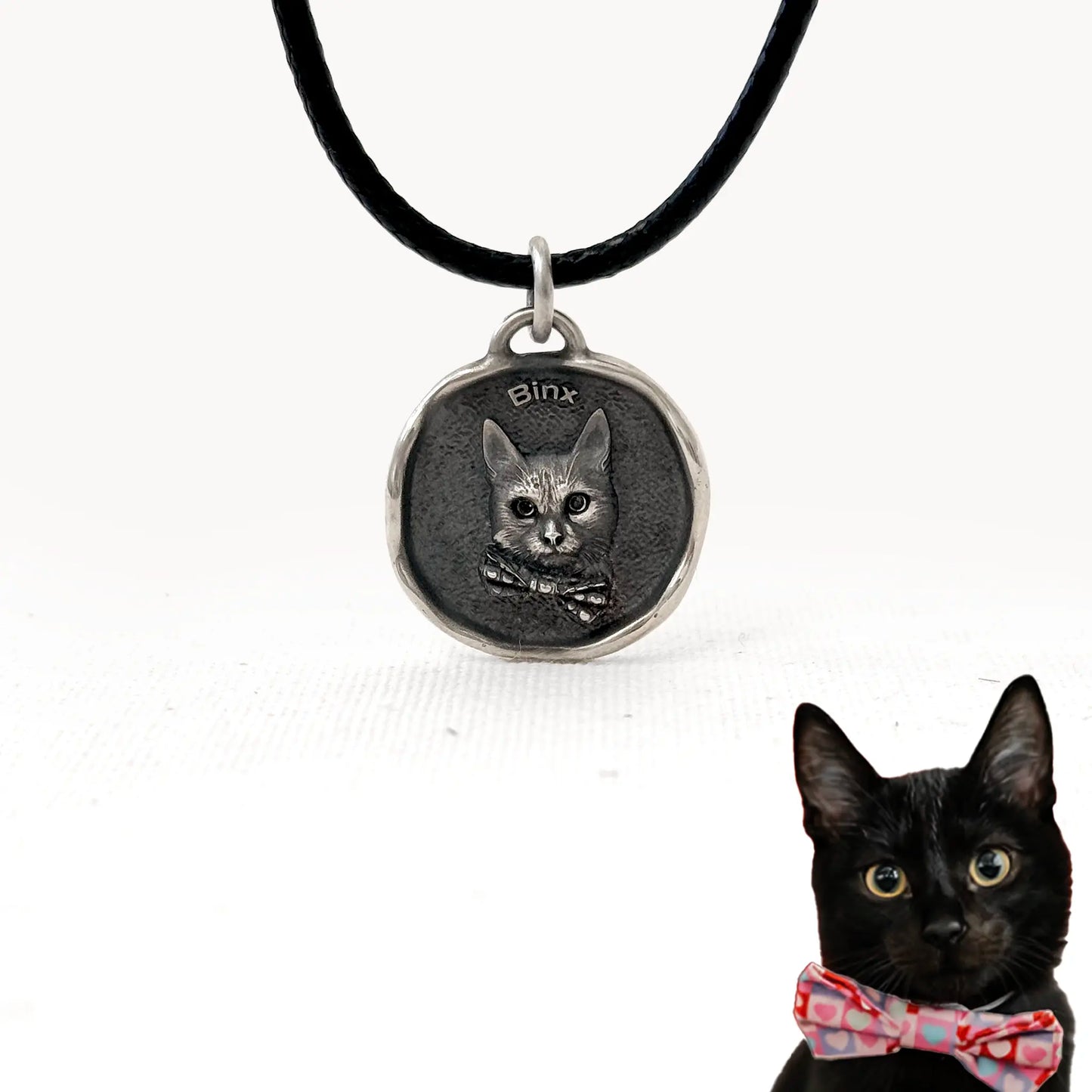 Custom silver cat pendant with engraved portrait of Binx, wearing a bow tie, on a black cord necklace.