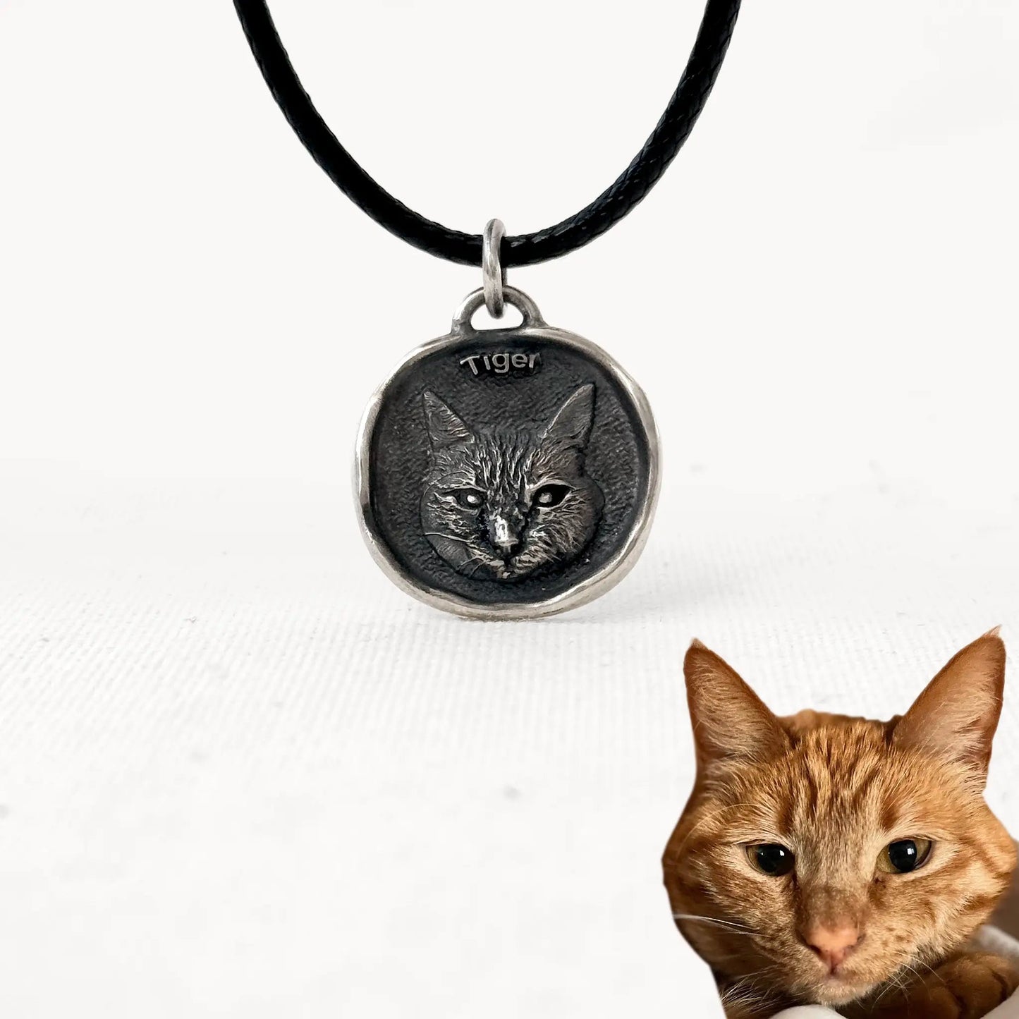 Custom silver cat pendant with engraved portrait of Tiger, ginger tabby cat, on a black cord necklace.