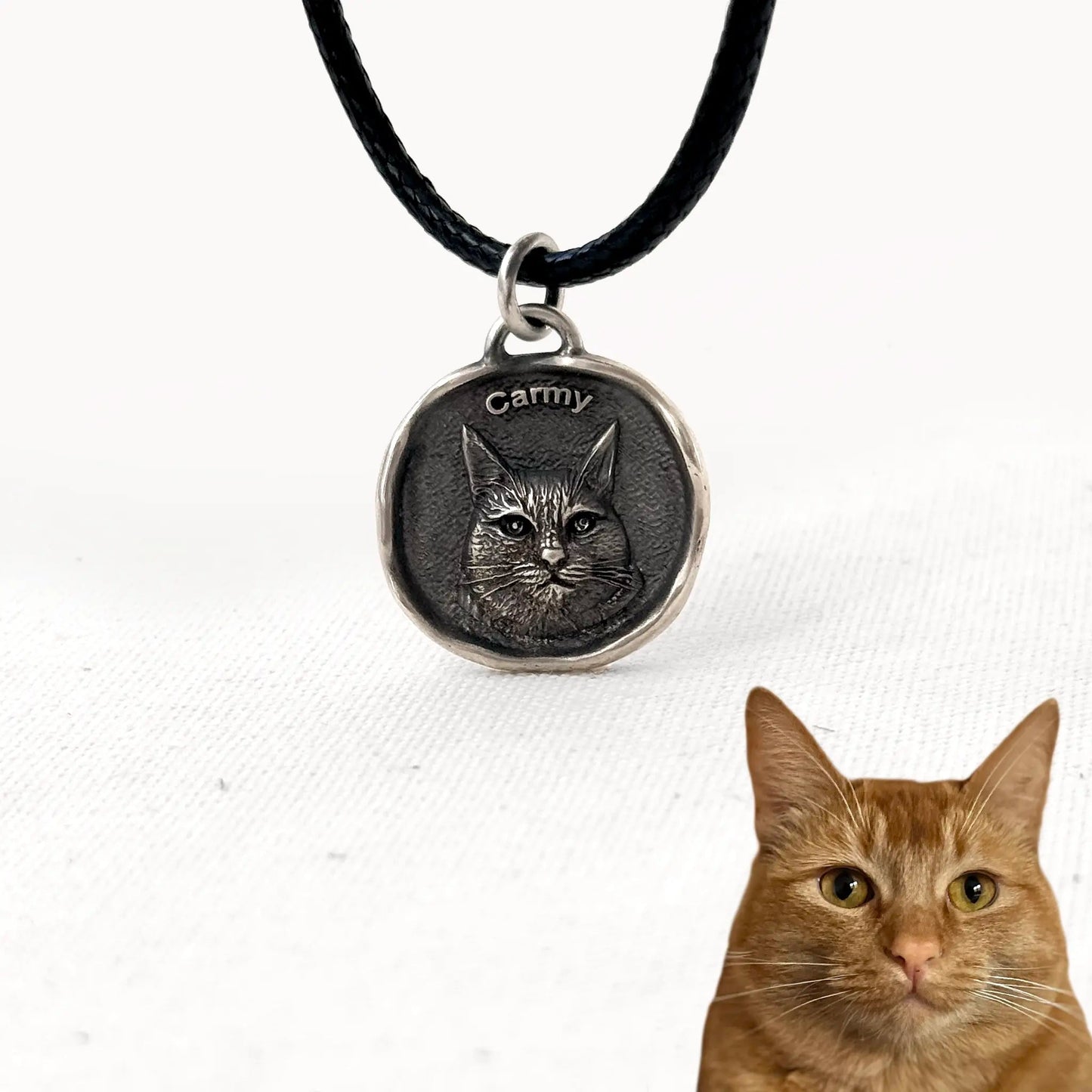 Custom silver cat pendant with engraved portrait of Carmy, ginger tabby cat, on a black cord necklace.