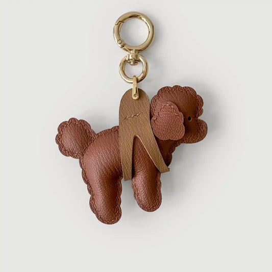 A brown textured leather poodle-shaped keychain charm with gold-tone metal hardware, shown on a light gray background.