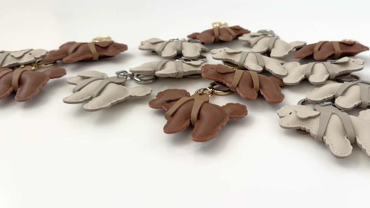 A set of small leather puppy-shaped keychains or charms in brown and light beige, arranged on a plain white surface.