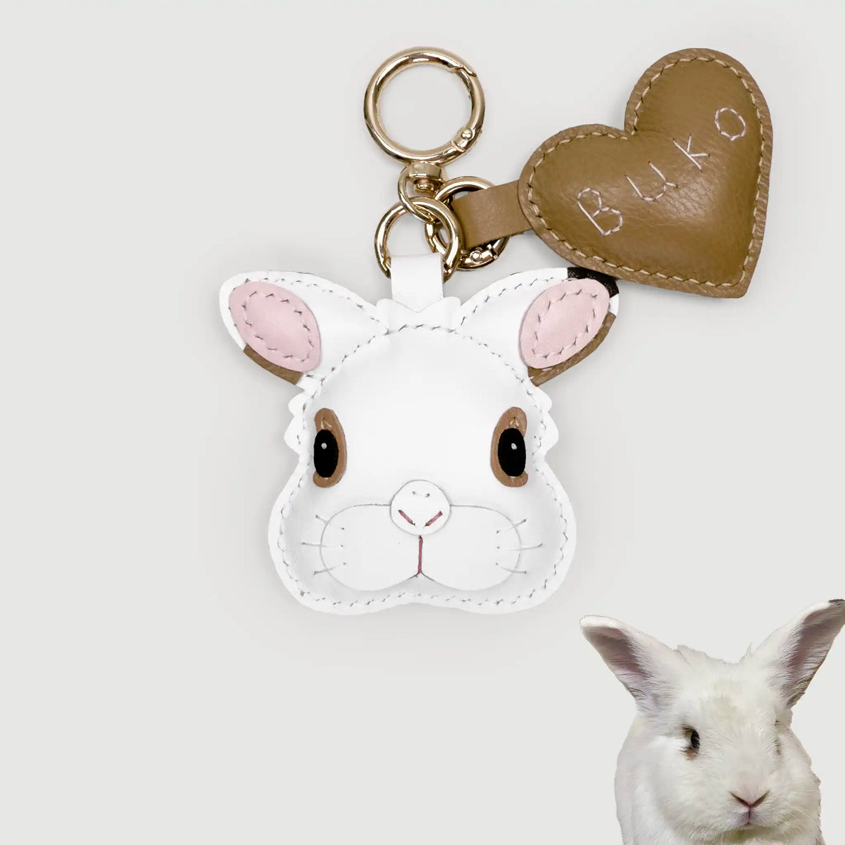 White rabbit-shaped keychain with pink ears and a heart-shaped tag on a light gray background.