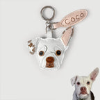 Custom pet leather keychain featuring a white French Bulldog head with brown embroidered details, a light pink ear tab with 'Coco' stitched in brown, and a silver key ring, shown against a light gray background with a small photo of the dog in the bottom right corner.