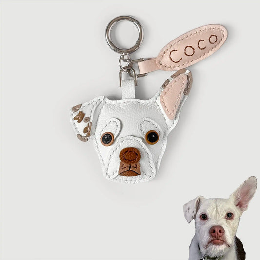 Custom pet leather keychain featuring a white French Bulldog head with brown embroidered details, a light pink ear tab with 'Coco' stitched in brown, and a silver key ring, shown against a light gray background with a small photo of the dog in the bottom right corner.