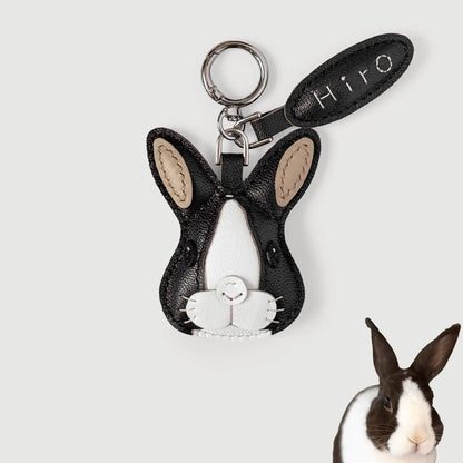 A black and white rabbit-shaped keychain charm with beige ear inlays and a silver key ring, shown on a light gray background with a small rabbit photo in the lower right corner. The leather tag reads 'Hiro'.