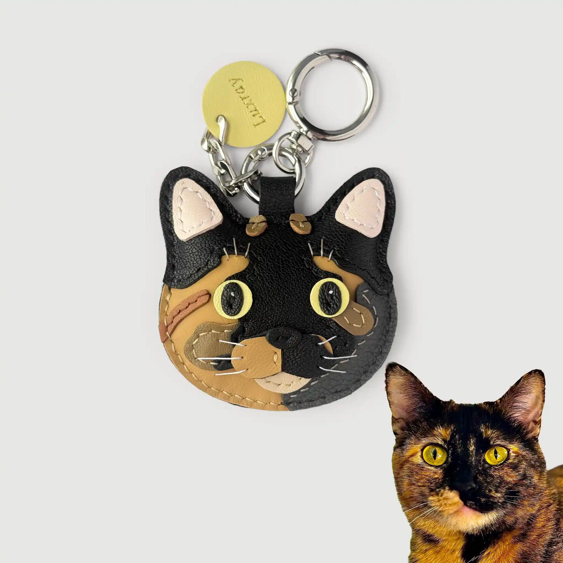 Cat-shaped keychain with a tortoiseshell cat next to it on a white background