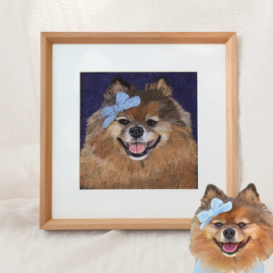 Custom-made wool felt pet portrait of Bella the Pomeranian, smiling with a blue bow, framed as soft-textured dog artwork.
