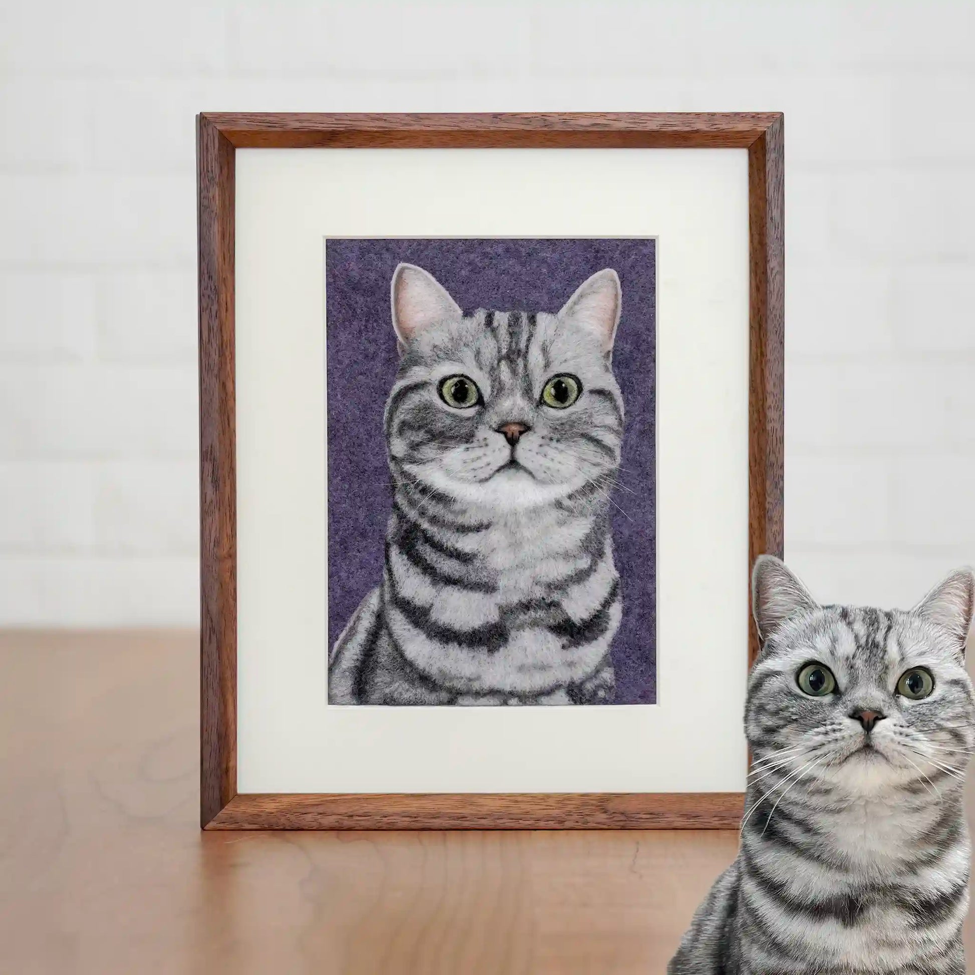 Wool felt portrait of Lianlian the silver American Shorthair, with green eyes and stripes, framed on a purple background.