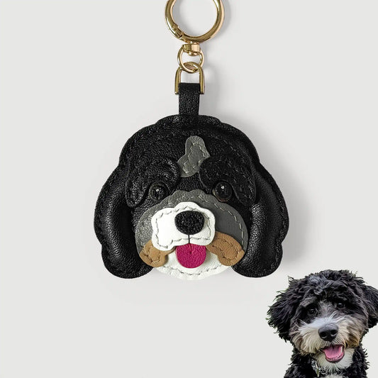 A black leather dog-shaped keychain charm with a gold key ring, shown on a light gray background with a small dog photo in the lower right corner.