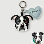 A custom dog keychain featuring a realistic black and white bulldog face with embroidered details, attached to a silver key ring and a light blue heart-shaped tag labeled 'Pepper'. A small inset photo of a real black and white dog wearing a green bandana is shown in the bottom right corner.