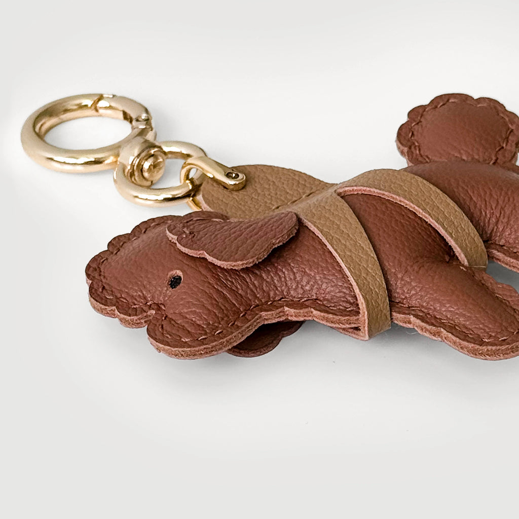 A brown leather dog-shaped keychain with a gold-tone split ring, shown on a light gray background.