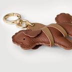 A brown leather dog-shaped keychain with a gold-tone split ring, shown on a light gray background.