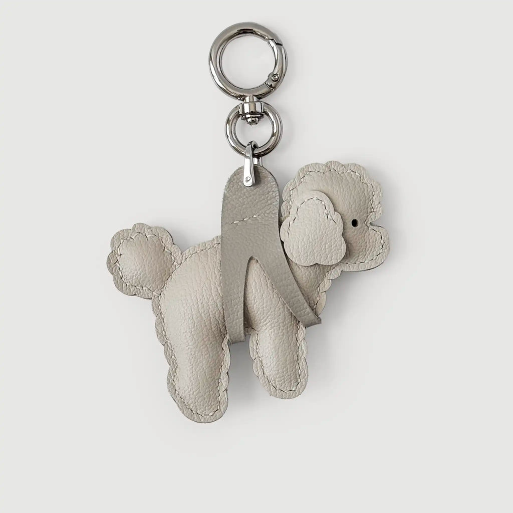 A light beige leather poodle-shaped keychain with a silver-tone metal key ring and split ring, shown on a light gray background.
