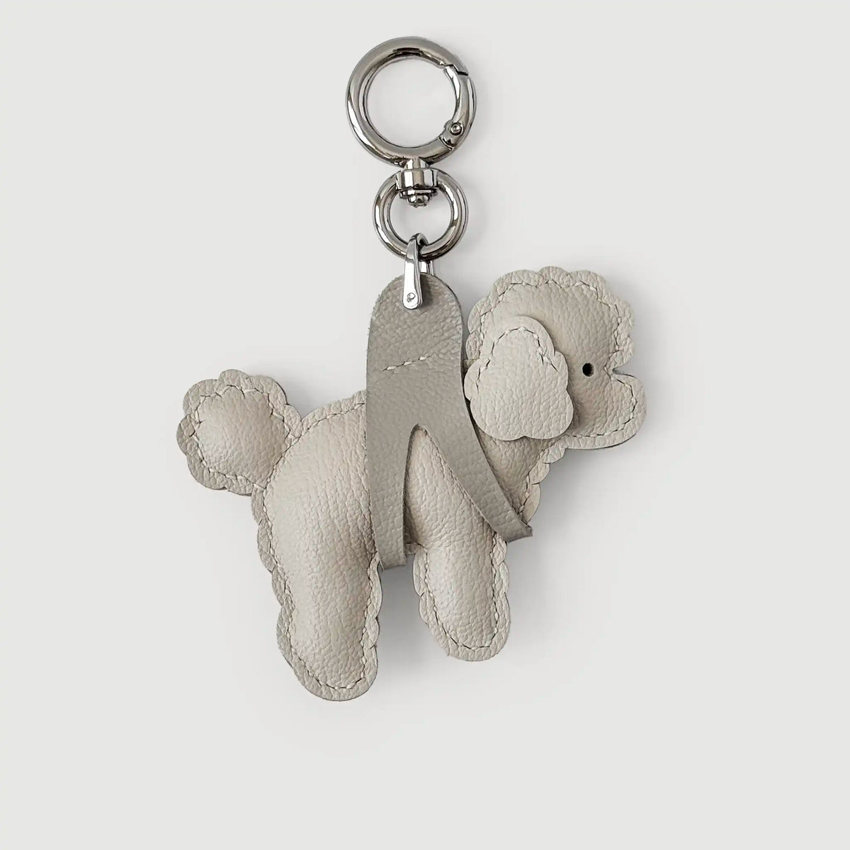 A light beige leather poodle-shaped keychain with a silver-tone metal key ring and split ring, shown on a light gray background.