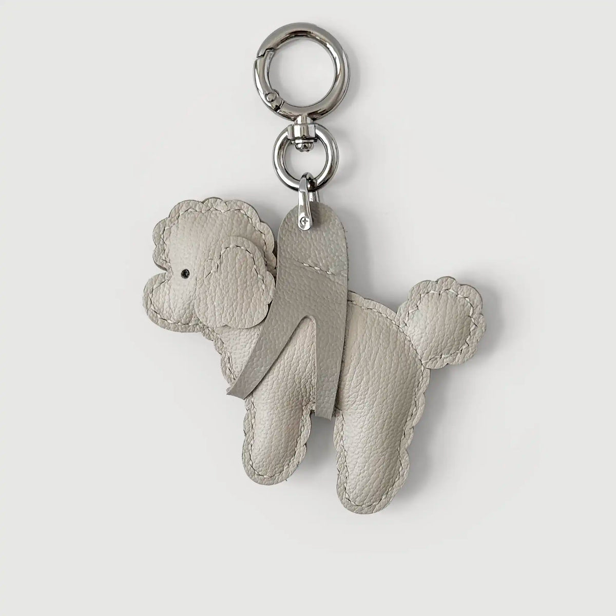 A light gray leather poodle-shaped keychain with a silver-tone split ring and key ring, shown on a light gray background.